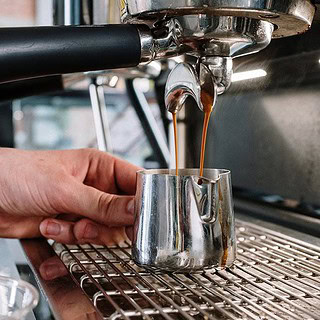 man sieht eine Siebträgermaschine, die einen Behälter mit Kaffee befüllt- Barista Basic Schulung in Dresden