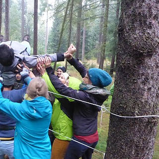 Gruppe hebt eine Person über ein Hindernis bei der Team Challenge Schnitzeljagd