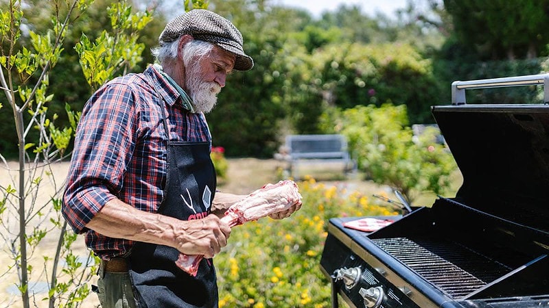 Ein Mann steht neben einem Grill und hält Fleisch in der Hand