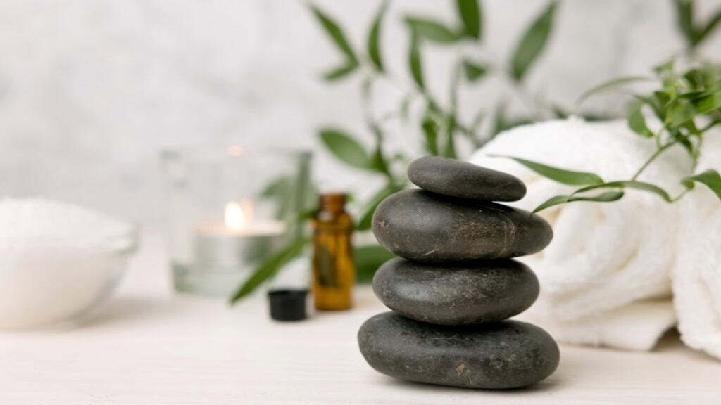 Hot Stone Massage-Vulkansteine Auf einer Massagebank liegen Vulkansteine und ein Handtuch und ätherische Öle - Hot Stone Massage