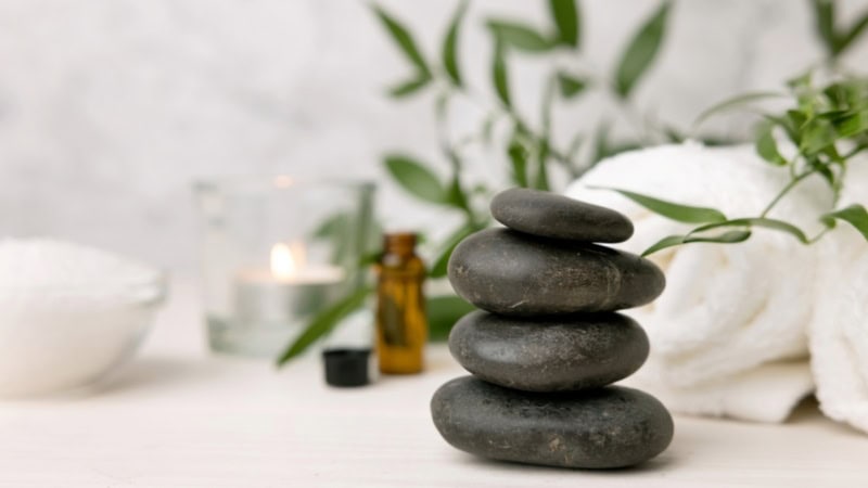Auf einer Massagebank liegen Vulkansteine und ein Handtuch und ätherische Öle - Hot Stone Massage