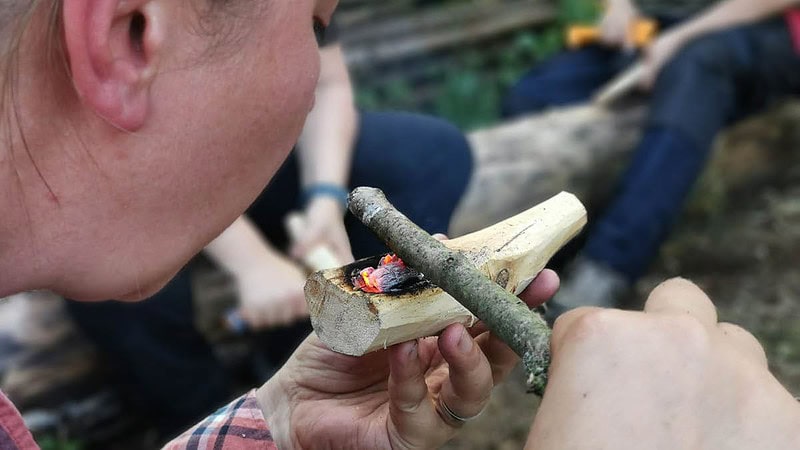 Frau entfacht Feuer mit klienem Holz.