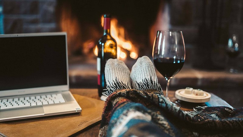 Eine Person sitzt am Computer am Tisch zu Hause und genießt Rotwein