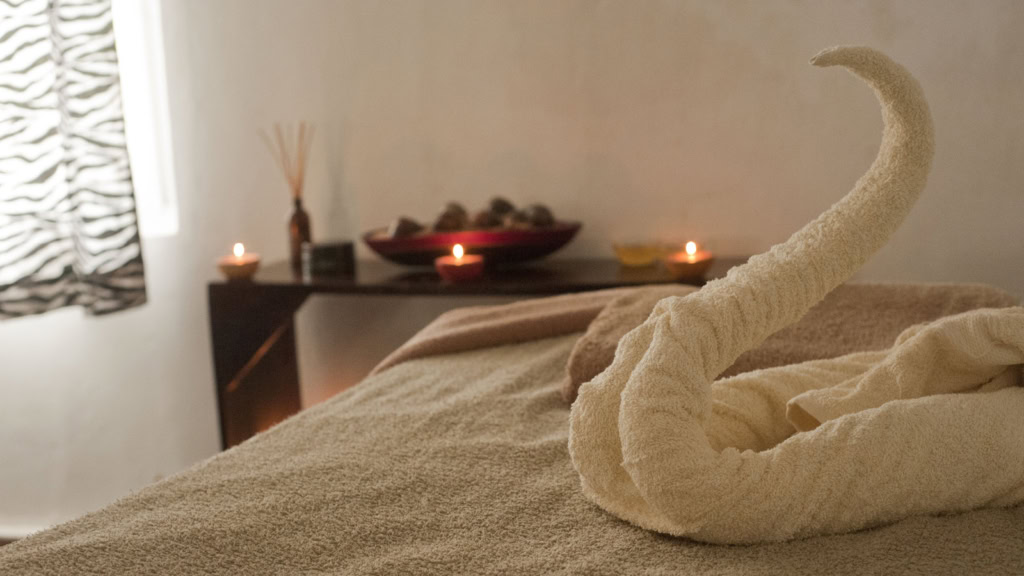 Handtuch zu einem Schwan gefaltet, Massageliege, Kerzen im Hintergrund