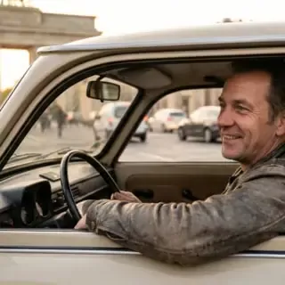 Mann sitzt in einem braunen Trabant 601 - das Brandenburger Tor im Hintergrund zu sehen