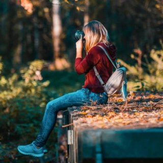Eine Frau sitzt auf einem Stein am Wald in der Sonne