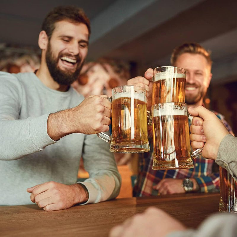 3 Männer feiern zusammen in einer Bar und stoßen mit Bier an