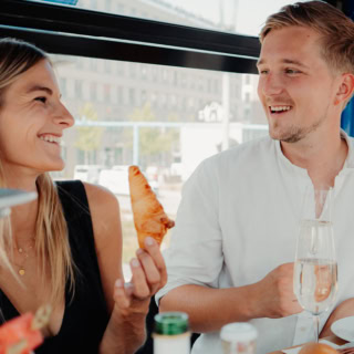 Frau und Mann sitzen in dem riesenrad in Dresden und frühstücken. Mann rechts hat ein weißes Hemd und die Frau ein schwarzes Oberteil an.