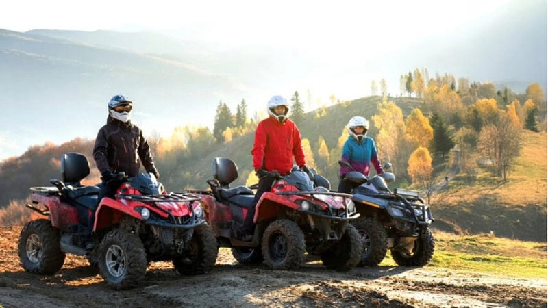 3 Quad Fahrer die auf ihren Quads auf einem Berg stehen.