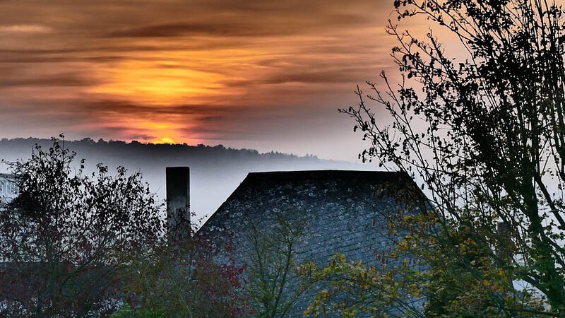 Dach eines Hauses mit Schornstein im Nebel des Waldes bei Sonnenaufgang