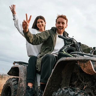 Ein Mann und eine Frau auf einen Quad die lachen und Peace mit ihren Händen zeigen.