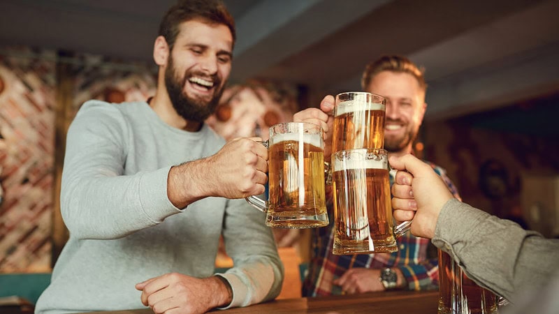 3 Männer feiern zusammen in einer Bar und stoßen mit Bier an