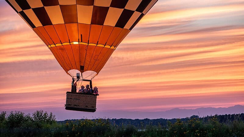 Menschen in einem bunten Ballon über einem Waldabschnitt bei Sonnenuntergang- Ballonfahrt- Menschen im Ballon