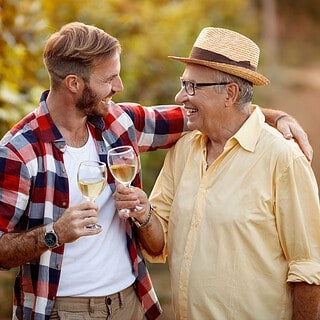 Vater und Sohn genießen bei einer gemeinsamen Weinwanderung ein Glas Weißwein.