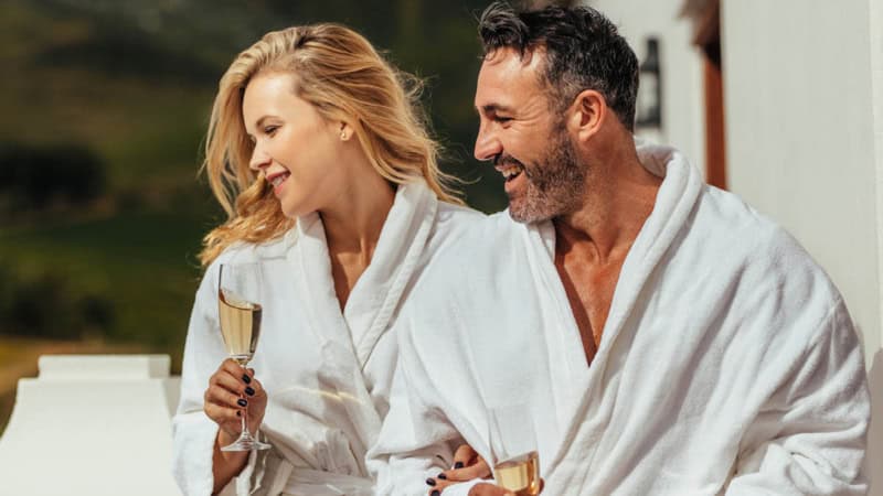 Ein Paar im Bademantel welches Champagner trinkt und lacht.