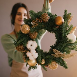 Eine Frau zeigt ihren selbstgemachten weihnachtlichen Kranz mit verschiedenen Dekorationen.
