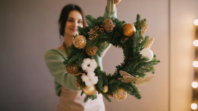 Eine Frau zeigt ihren selbstgemachten weihnachtlichen Kranz mit verschiedenen Dekorationen.