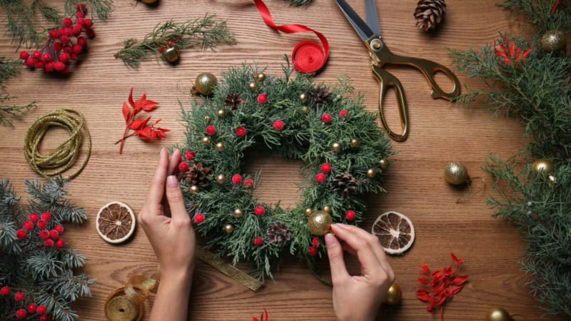 Ein weihnachtlicher Kranz wird auf einem Tisch mit verschiedenen Adventsdekorationen schmückt.