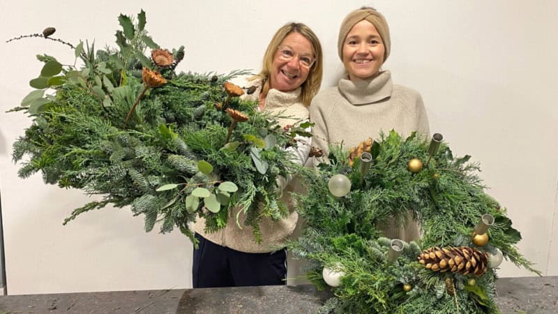 2 Frauen zeigen ihre selbstgemachte Adventkränze und lächeln.