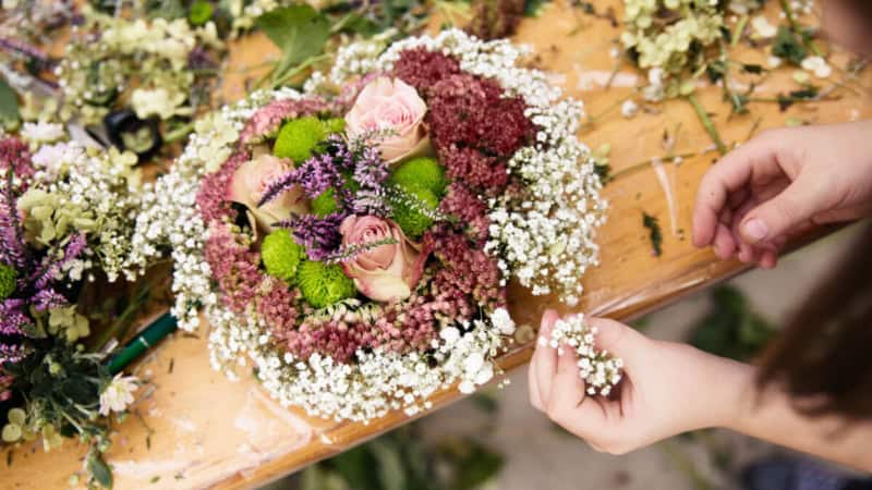 Eine Person nimmt an einem Floristikkurs teil und lernt wie man Blumenkränze bindet.