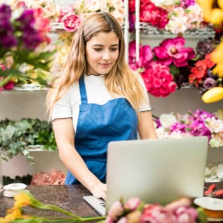 Eine Frau nimmt an einem Floristikkurs in einem Blumenladen teil. Viele verschiedene Blumensorten befinden sich im Hintergrund.