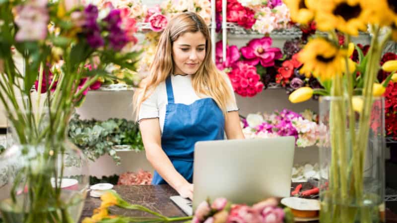 Eine Frau nimmt an einem Floristikkurs in einem Blumenladen teil. Viele verschiedene Blumensorten befinden sich im Hintergrund.