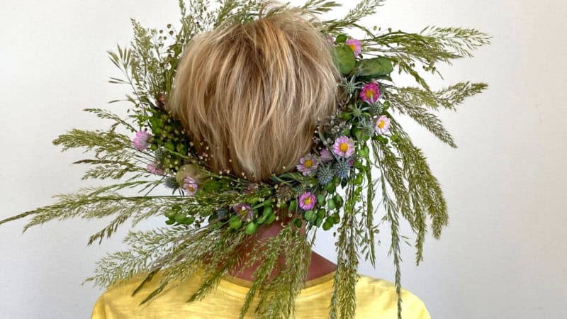 Eine Frau trägt einen großen Kranz aus Blumen und Pflanzen.