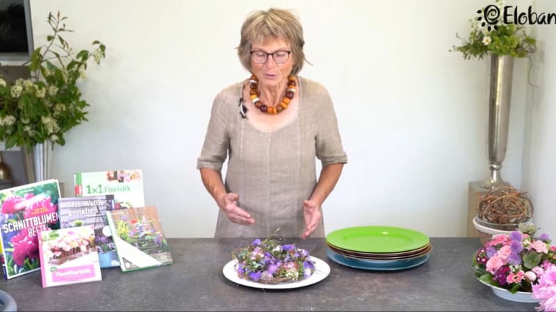 Eine Frau erklärt während des Floristikkurses wie man einen Blumenkranz zusammenstellt.