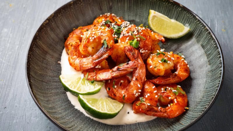 Gegrillte Tandoori Garnelen mit Limetten und Mayonnaise auf einem Teller.