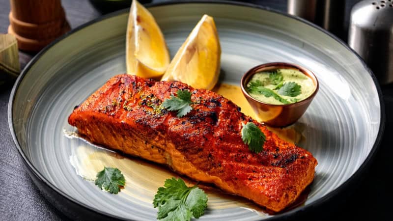Gegrillter Tandoori Lachs mit Gemüse und Soße auf einem Teller.