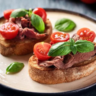 Mediterrane Brötchen mit Fleisch, Tomaten und Basilikum auf einem Teller.