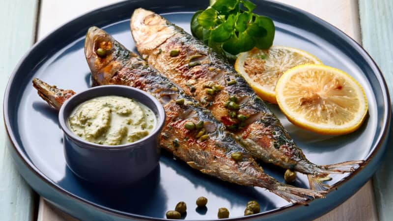 Gegrillte Fische mit Gemüse und Soße auf einem Teller.
