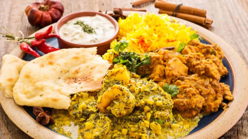 Indisches Hänchen Tikka Masala mit Gemüse und Soße auf einem Teller aus Holz.