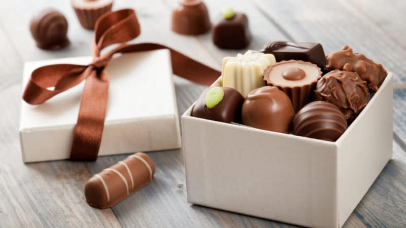 Eine Box mit Schokoladenpralinen, mehr Pralinen im Hintergrund.