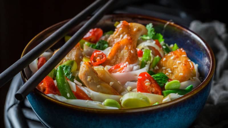 Thai Gericht mit Fleisch und Gemüse mit Stäbchen in einem Schüssel.