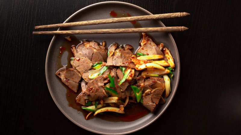 Thailändische Speise mit Fleisch und Gemüse auf einem Teller mit Stäbchen.