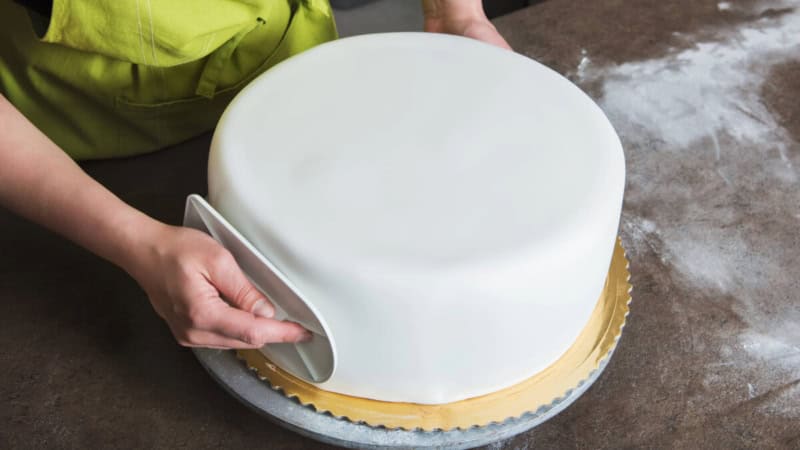 Eine Frau lernt, wie man eine Torte mit Fondanttechnik dekoriert.