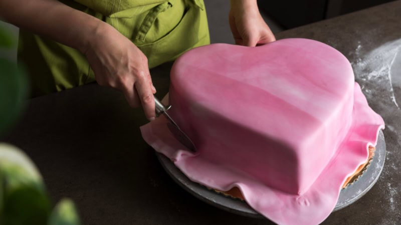 Eine Frau dekoriert eine Torte im Herzform mit Fondant.
