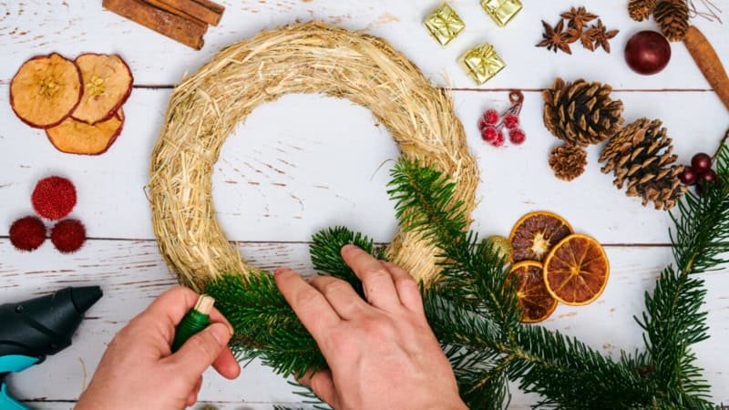 Eine Person stellt einen winterlichen Kranz auf einem Tisch zusammen, es liegen verschiedene Dekorationen auf dem Tisch.