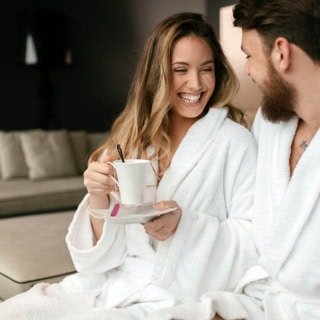 Ein Paar welches im Bademantel Tee trinkt und lacht.