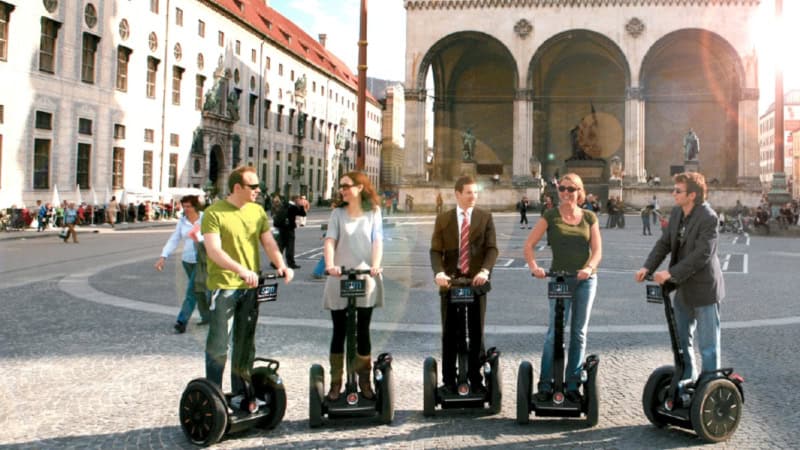 Segway Tour Teilnehmer posieren für ein Gruppenfoto in München, auf dem Odeonsplatz, die Sonne scheint.