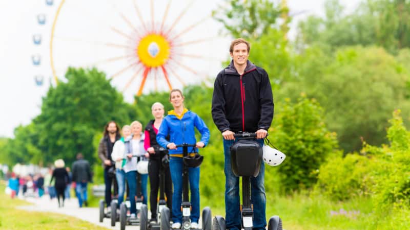 Eine Gruppe fährt auf den Segways in München, das Riesenrad ist im Hintergrund zu sehen.