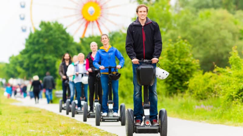 Eine Gruppe fährt auf den Segways in Regensburg, das Riesenrad ist im Hintergrund zu sehen.