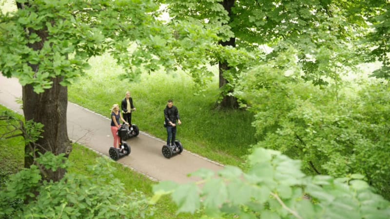 3 Teilnehmer von einer Segway-Tour-Gruppe fahren durch den Park in Stuttgart auf den Segways.