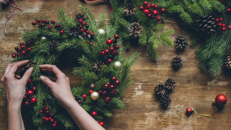Eine Frau bindet einen weihnachtlichen Kranz beim Advent-Kranzseminar.