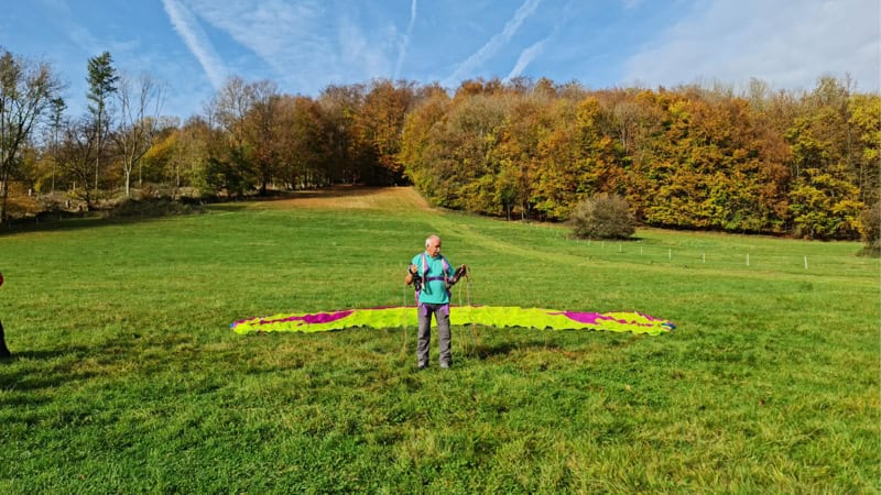 Kursleiter erklärt beim Drachen und Gleitschirmkurs am Hang etwas. Hintergrund Bäume