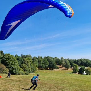 blauer Gleitschirm und unten ein Mann hängt daran