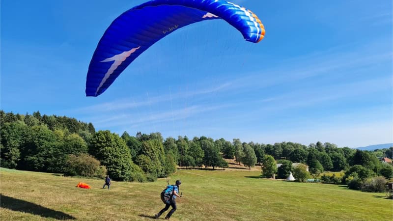 blauer Gleitschirm und unten ein Mann hängt daran