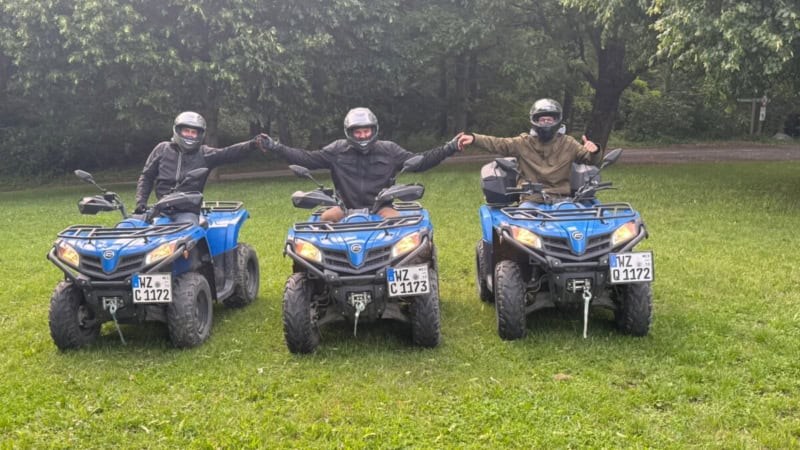 Drei Teilnehmer einer Quad Tour posieren gemeinsam auf ihren Quads und halten sich an den Händen.