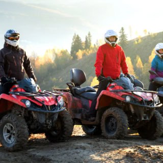 Drei Quad-Fahrer sitzen auf ihren Quads in der Sonne, im Hintergrund dichter Wald.